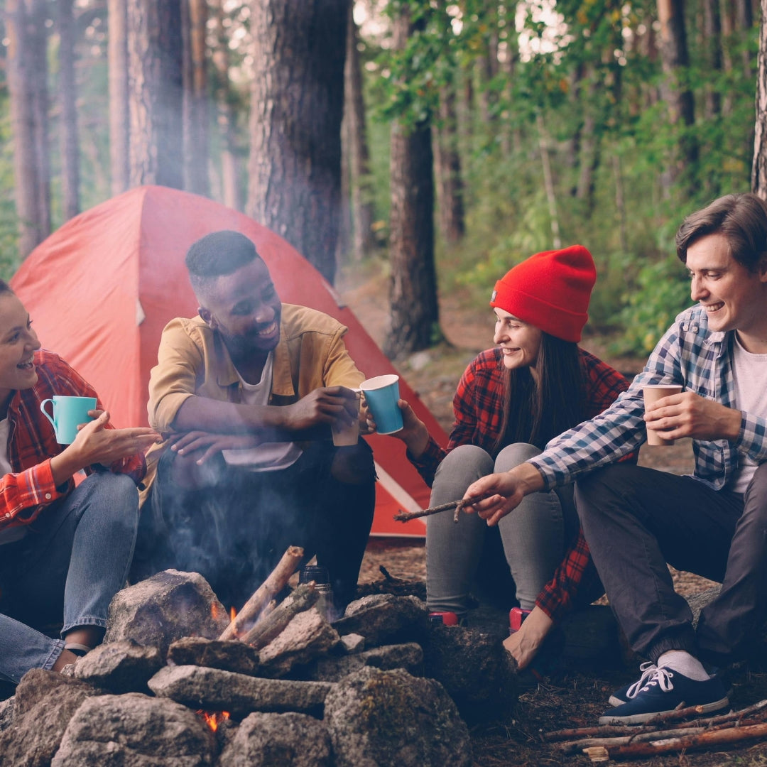 Group of friends sitting around a campfire with a tent in the background