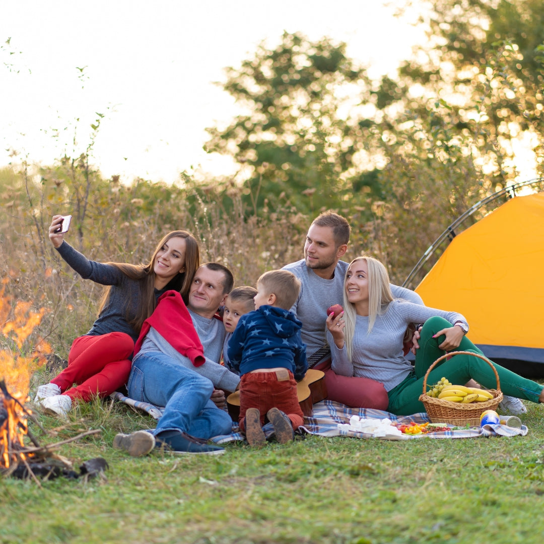 Family of five taking a selfie by a campfire with a yellow tent in the background.