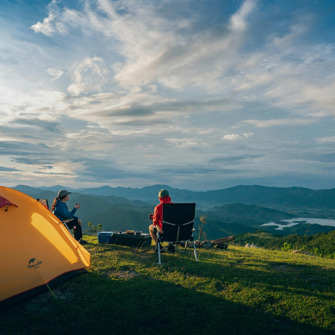 Two people camping on a mountain with a scenic view of mountains and clouds.